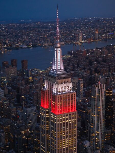 Imponujące ujęcie słynnego Empire State Building po zmroku, z lotu ptaka, z panoramą Nowego Jorku. Wieżowiec jest oświetlony w polskie barwy narodowe – szczyt w kolorze białym, a środkowa część w czerwonym. To właśnie światła, które uroczyście włączyli Lewandowscy na Empire State Building z okazji 11 listopada, stanowiąc widoczny symbol polskiej dumy w sercu USA.