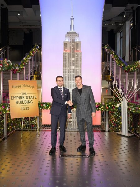 Zdjęcie przedstawia Roberta Lewandowskiego w towarzystwie Konsula Generalnego RP w Nowym Jorku. Mężczyźni w eleganckich garniturach ściskają sobie dłonie, stojąc w świątecznie udekorowanym holu Empire State Building. To spotkanie miało miejsce przed symbolicznym włączeniem świateł na wieżowcu, będącym częścią uczczenia polskiego Święta Niepodległości.