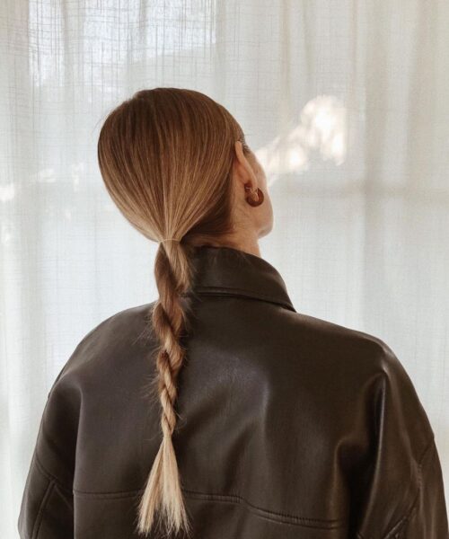 Kadr z tyłu przedstawia kobietę w brązowej skórzanej kurtce, której długie włosy są ściągnięte w niski, gładki kucyk, a następnie zaplecione w gruby warkocz. Włosy, cieniowane od brązu do blondu, prezentują się na tym ujęciu na bardzo gęste i mocne.