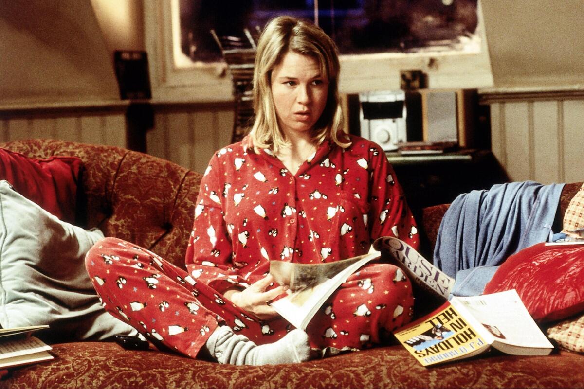 Filmy na poprawę humoru. Aktorka Renée Zellweger jako Bridget Jones siedzi na kanapie w domu w charakterystycznej, czerwonej piżamie w białe pingwiny i szarych skarpetkach. Trzyma w rękach otwarte czasopismo lub książkę i patrzy przed siebie z lekko zatroskaną miną. Scena pochodzi z filmu "Dziennik Bridget Jones".