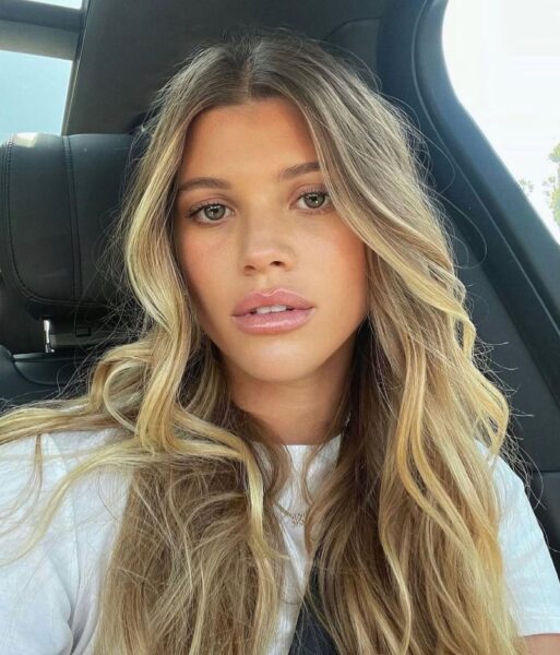 Ujęcie zbliżone przedstawia młodą kobietę z długimi, falowanymi, blond włosami, siedzącą na czarnym fotelu we wnętrzu samochodu. Ma na sobie białą koszulkę i patrzy bezpośrednio w obiektyw, a jej pełne usta i naturalny makijaż stanowią jej wizytówkę. Choć jej estetyka jest nieskazitelna, pielęgnacja urody musi iść w parze ze zdrowiem, szczególnie w kontekście kuracji odchudzających. Osoby stosujące popularne leki, które mogą prowadzić do suchości w jamie ustnej, muszą dbać o zęby szczególnie, aby uniknąć problemów określanych jako zęby po Ozempicu.