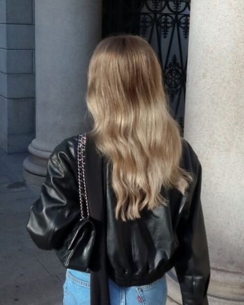 Kobieta o pięknych, lśniących blond włosach idąca na zewnątrz. Jej włosy wyglądają zdrowo pomimo niesprzyjających warunków – to przykład tego, jak dbać o włosy zimą, żeby nie straciły blasku.