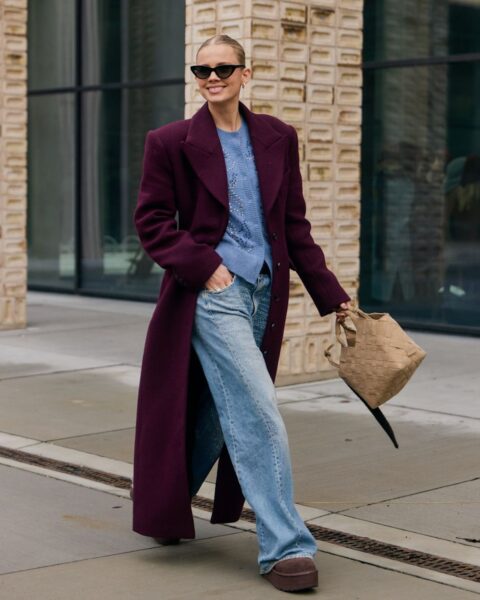 Stylizacja street fashion z Kopenhagi. Kobieta w długim, burgundowym płaszczu z szerokimi, wyrazistymi ramionami, błękitnym sweterku i szerokich jeansach zdobionych kryształkami. Całość uzupełniają platformy w kolorze brązowym, mała, pleciona torebka typu koszyk w kolorze beżowym oraz czarne, kocie okulary przeciwsłoneczne. Płaszcz maxi damski – inspiracja kolorystyczna na jesień.