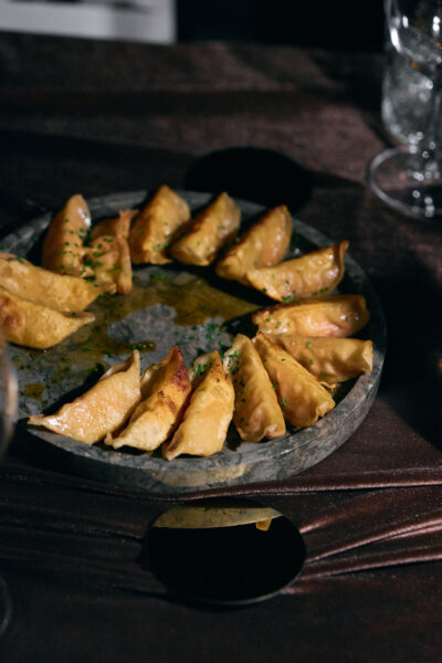 Okrągły talerz wypełniony chrupiącymi pierożkami gyoza, ułożonymi w okrąg i polanymi aromatycznym sosem, ustawiony na brązowym, błyszczącym obrusie podczas wieczornej kolacji.