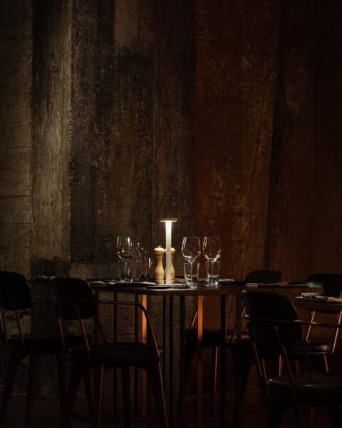 Nastrojowe wnętrze restauracji z przyciemnionym światłem i elegancko nakrytymi stolikami sprzyja spokojnemu świątecznemu spotkaniu. Taki klimat idealnie pasuje do restauracji otwartej w pierwszy dzień świąt w Warszawie, oferującej uroczystą kolację w kameralnej atmosferze.