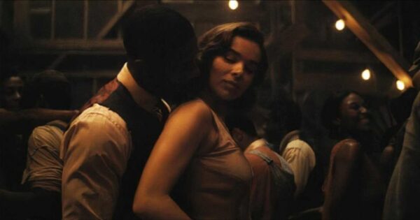 Kadr z filmu Grzesznicy. Bliskie ujęcie tańczącej pary na tle rozświetlonej girlandami sali, gdzie mężczyzna w ciemnej kamizelce szepcze do ucha kobiety o jasnych, falujących włosach, w białej bluzce. Intymny nastrój i vintage'owa estetyka tego dramatycznego kadru przypominają wizualną dbałość, jakiej oczekujemy od najlepszych filmów 2025 roku. Ta pełna emocji scena miłosnego tańca to zapowiedź głębokiej historii, która ma szansę stać się kinowym hitem przyszłego sezonu.