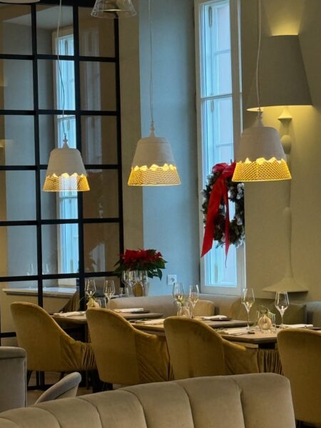 Eleganckie wnętrze restauracji z miękkim oświetleniem, świątecznym wiankiem i starannie nakrytymi stołami tworzy spokojną, uroczystą atmosferę sprzyjającą długim rozmowom. Taki wystrój idealnie pasuje do restauracji otwartej w Boże Narodzenie 2025 w Warszawie, gdzie 25 grudnia można celebrować pierwszy dzień świąt w komfortowym, stylowym otoczeniu.