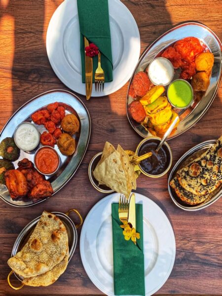 Stół pełen indyjskich przekąsek, curry, chlebków naan i sosów, przygotowany do wspólnego biesiadowania w restauracyjnym wnętrzu. Tak prezentują się propozycje, jakie serwują restauracje otwarte w drugi dzień świąt w Warszawie, oferujące aromatyczne dania zamiast klasycznego świątecznego menu. To dobra opcja na spotkanie z bliskimi poza domem po świętach.