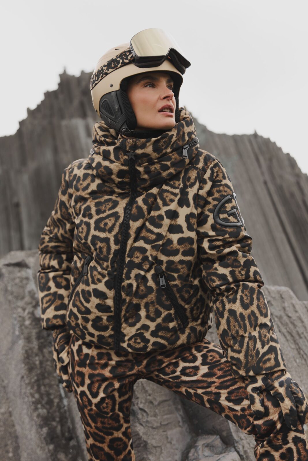 Kampania S’portofino zima 2025/2026: Kobieta w kombinezonie narciarskim w panterkę, z kaskiem i goglami, pozująca na tle skalnego pejzażu; odważna zimowa stylizacja łącząca modowy print z techniczną odzieżą sportową.