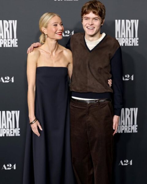 Gwiazda Hollywood Gwyneth Paltrow w stylowej sukience kopertowej w żółto-granatowe pasy i boho wzory, pozuje z córką Apple i synem Mosesem w swobodnych, letnich stylizacjach. Apple ubrana jest w delikatną, białą sukienkę na ramiączkach, a Moses w białą, casualową koszulkę. Zdjęcie w letnim, beztroskim klimacie, idealne jako inspiracja mody rodzinnej na wakacje.