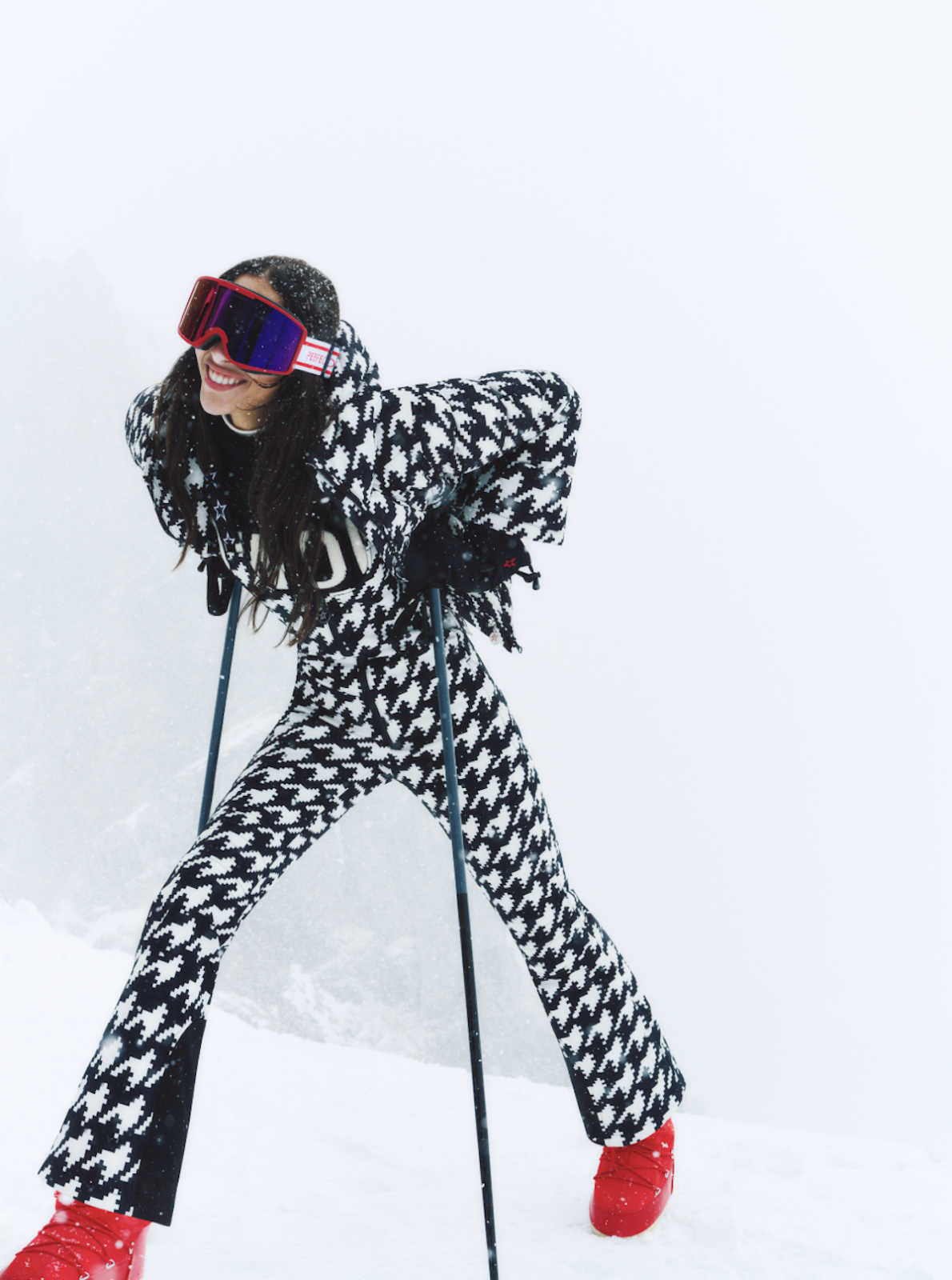 S'portofino narciarski power dressing: Dynamiczne ujęcie modelki w czarno-białym, graficznym kombinezonie narciarskim, czerwonych butach i goglach; pochylona sylwetka i śnieżne tło podkreślają ruch oraz sportową energię stylizacji.
