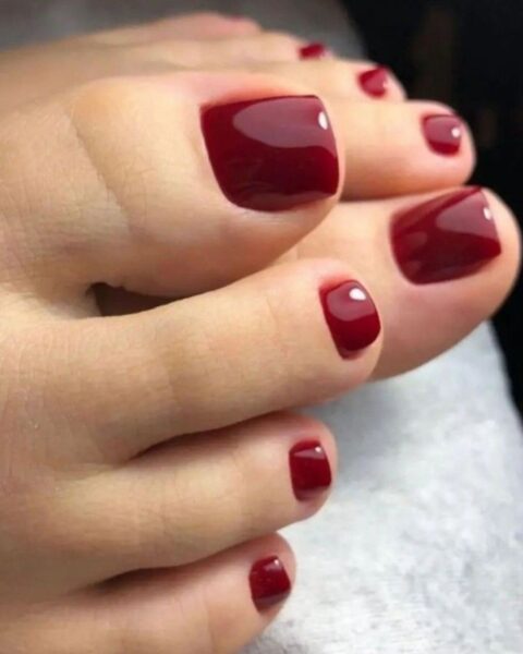 Dwa zdjęcia prezentujące luksusowy żurawinowy pedicure w głębokim odcieniu bordo. Na pierwszym zdjęciu widać także dłonie z pasującym manikiurem, podkreślającym trend 'matchy-matchy' w stylizacji paznokci u dłoni i stóp.