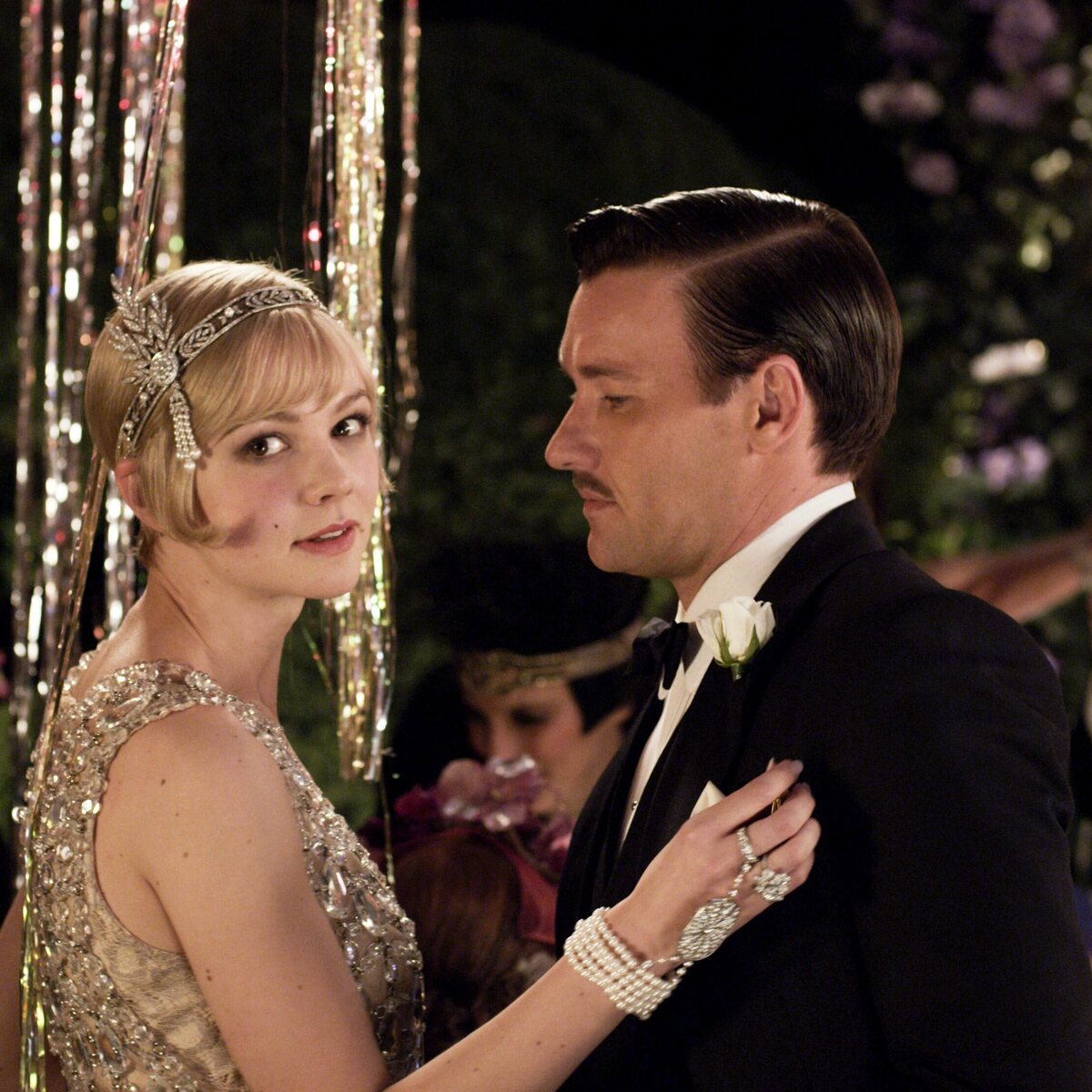 Filmy idealne na przerwę świąteczno-noworoczną. Kadr z filmu „Wielki Gatsby” przedstawiający bohaterów w eleganckich strojach z epoki lat 20., podczas wystawnego przyjęcia pełnego blasku i emocji. To właśnie takie sceny sprawiają, że ten tytuł regularnie wraca w zestawieniach jako filmy idealne na przerwę świąteczno-noworoczną. Produkcja doskonale nadaje się na spokojny seans w wolne dni, gdy szuka się klimatu, stylu i znajomej historii.