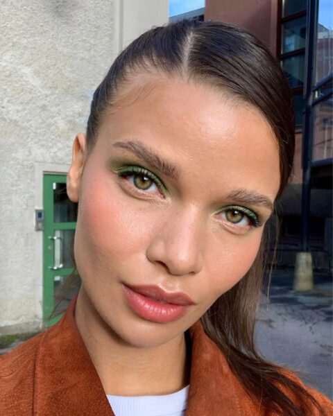 Na tym portrecie zbliżeniowym uwagę przykuwa żywy, intensywny zielony cień na powiekach, tworzący jednolity, graficzny akcent kolorystyczny. Reszta makijażu jest stonowana – skóra jest promienna, a policzki podkreślone różem, co idealnie dopełnia mocny kolor na oczach. Takie wykorzystanie śmiałych, nasyconych barw na powiekach to jeden z wyznaczników, jakie prezentują nadchodzące trendy w makijażu 2026.