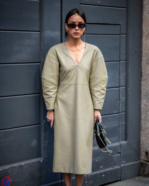 Kobieta w nowoczesnej, oliwkowej sukience midi z ekoskóry o rzeźbiarskim kroju z bufiastymi rękawami, zestawionej z sandałami w panterkę i czarną torebką do ręki – inspiracja na oryginalną stylizację w duchu minimalistycznego luksusu.