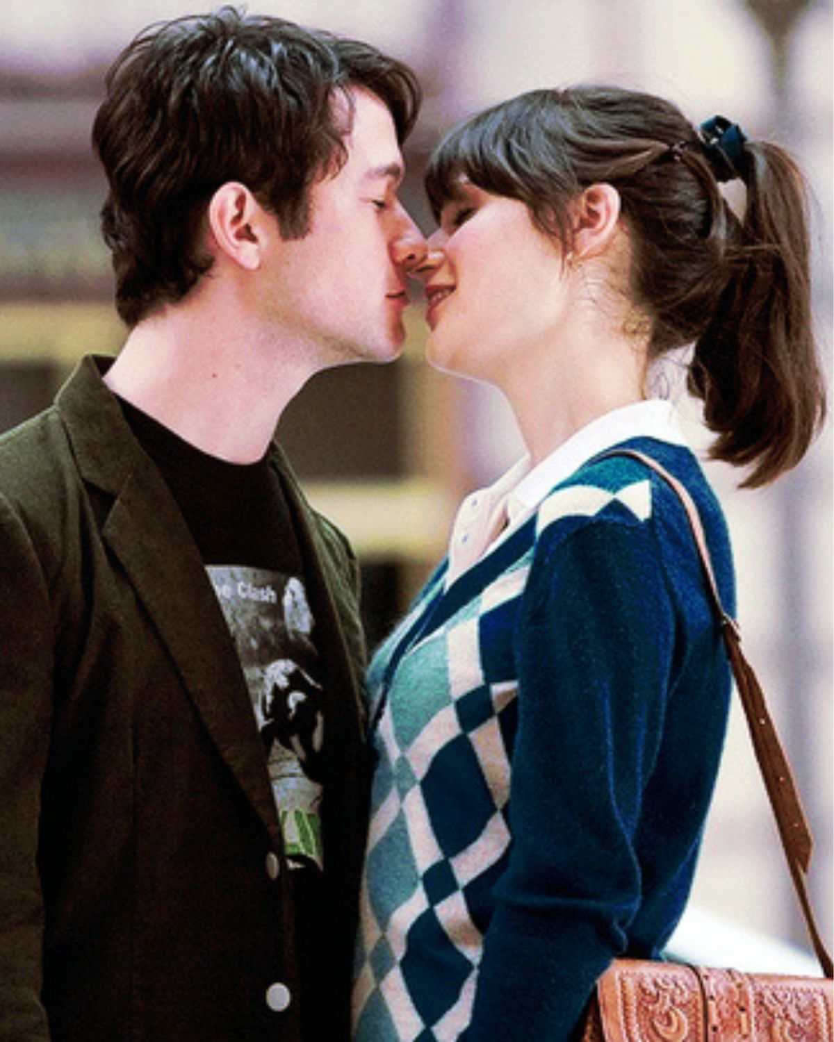Kadr z filmu „500 dni miłości” przedstawiający Zooey Deschanel i Josepha Gordona-Levitta w bliskim ujęciu, tuż przed pocałunkiem. Bohaterka ma na sobie niebieski kardigan w romby, a bohater ciemną marynarkę. Zdjęcie ilustruje temat: komedie romantyczne, które musisz znać.
