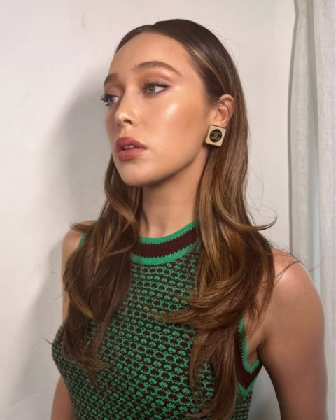 Portret Alycii Debnam-Carey z profilu w kolczykach Chanel, prezentującej modny kolor włosów brązowe złoto z elegancko wywiniętymi końcówkami i świetlistym makijażem.