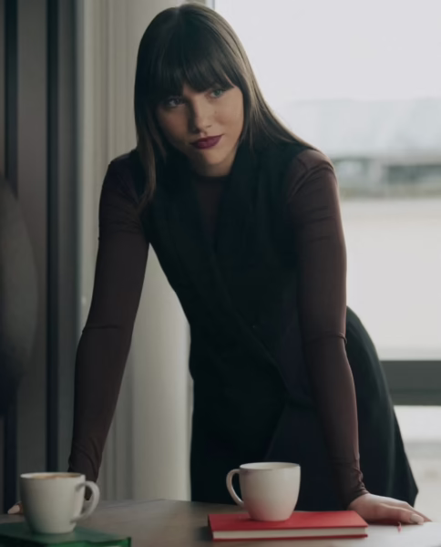 Mila Jankowska opiera się o stół w jasnym, nowoczesnym wnętrzu, ubrana w dopasowaną, ciemną sukienkę, spoglądając w bok z skupionym wyrazem twarzy. Kadr ma filmowy, intymny charakter i przywołuje skojarzenia z narracją serialową oraz rolami opartymi na napięciu i relacji.