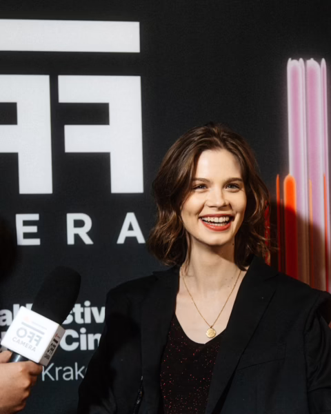 Matylda Giegżno uśmiecha się podczas wywiadu na tle festiwalowej ścianki, ubrana w czarną marynarkę i delikatną biżuterię. Zdjęcie oddaje jej profesjonalną, swobodną obecność w przestrzeni branżowej i moment, w którym coraz częściej pojawia się na wydarzeniach filmowych. To jedna z postaci zestawienia Młode polskie aktorki, które warto obserwować w 2026 roku.