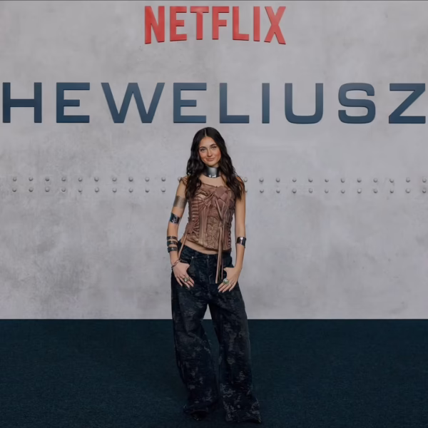 Mia Goti pozuje na premierze serialu „Heweliusz” na tle ściany z logo Netflixa, ubrana w stylizację inspirowaną estetyką Y2K z metalicznymi dodatkami. Zdjęcie podkreśla jej pewną, sceniczną obecność i moment wejścia do dużych produkcji platformowych.