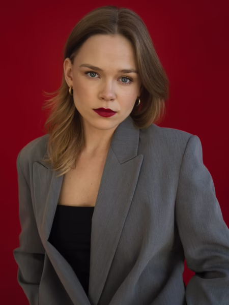 Agata Łabno pozuje na tle intensywnie czerwonej ściany, ubrana w szarą marynarkę i minimalistyczną stylizację, patrząc prosto w obiektyw. Portret ma formalny, wyważony charakter i podkreśla jej dojrzałą, świadomą obecność przed kamerą. To jedna z bohaterek zestawienia Młode polskie aktorki, które warto obserwować w 2026 roku.