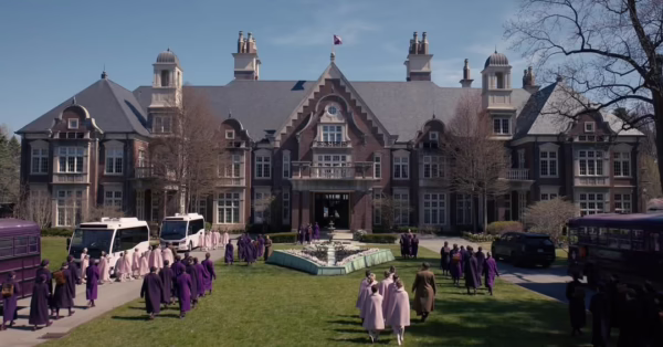 Kadr z serialu „The Testaments” ukazuje monumentalny budynek otoczony ogrodem, przed którym gromadzą się grupy kobiet i dzieci ubranych w jednolite, surowe stroje charakterystyczne dla porządku postgileadowego. Symetryczna kompozycja i chłodna skala przestrzeni podkreślają kontrolę, hierarchię i pozorny spokój świata po upadku reżimu. To jedno z ujęć zapowiadających najbardziej wyczekiwane seriale 2026, skupione na konsekwencjach ideologii i pamięci zbiorowej.