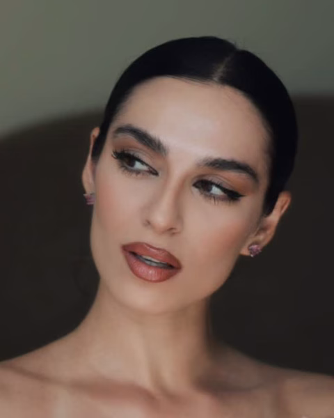 Portret kobiety o ciemnych włosach w gładkim upięciu, prezentującej elegancki makijaż typu smoky eye w odcieniach brązu oraz usta w kolorze stonowanej czerwieni. Zdjęcie w estetyce „quiet luxury” z widocznym tekstem o komforcie bycia ze samą sobą.