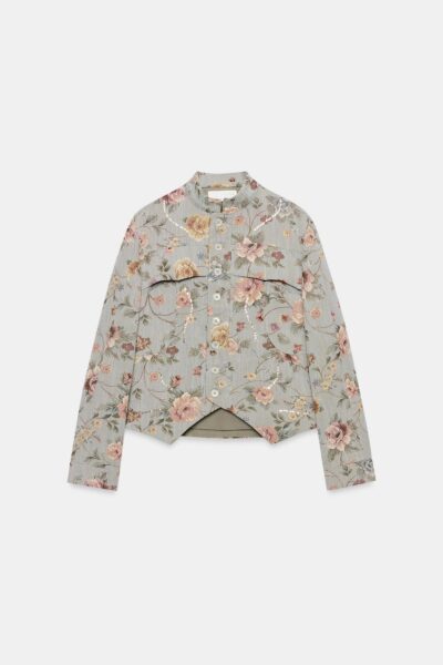 Zdjęcie produktowe krótkiej żakardowej marynarki Zara w kwiatowy wzór. Model ma jasnoszare tło, stonowane różowe i beżowe kwiaty, stójkę oraz zapięcie na guziki. Asymetryczne wykończenie dołu i subtelne zdobienia nadają marynarce romantyczny, dekoracyjny charakter.